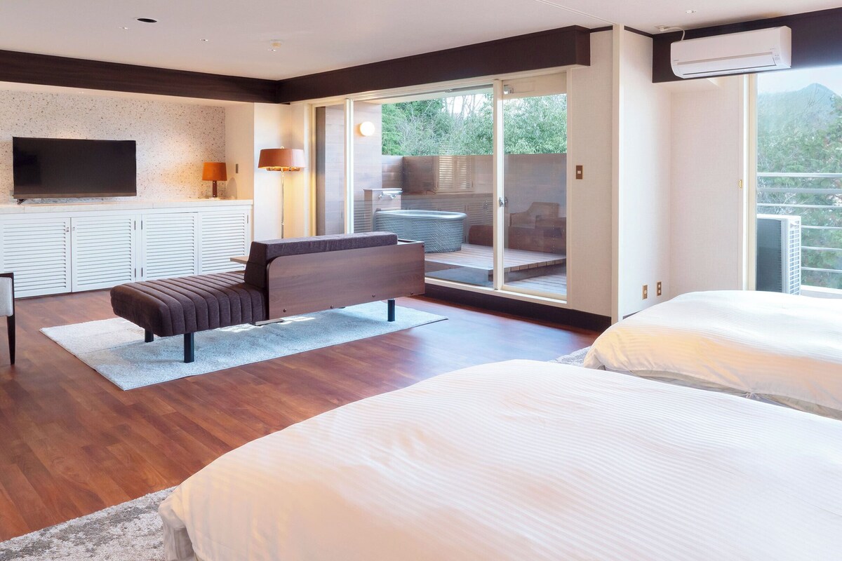 Ein modernes Hotelzimmer mit einem großen Bett, einem Sofa, einem Fernseher und einem Balkon mit Blick ins Freie.