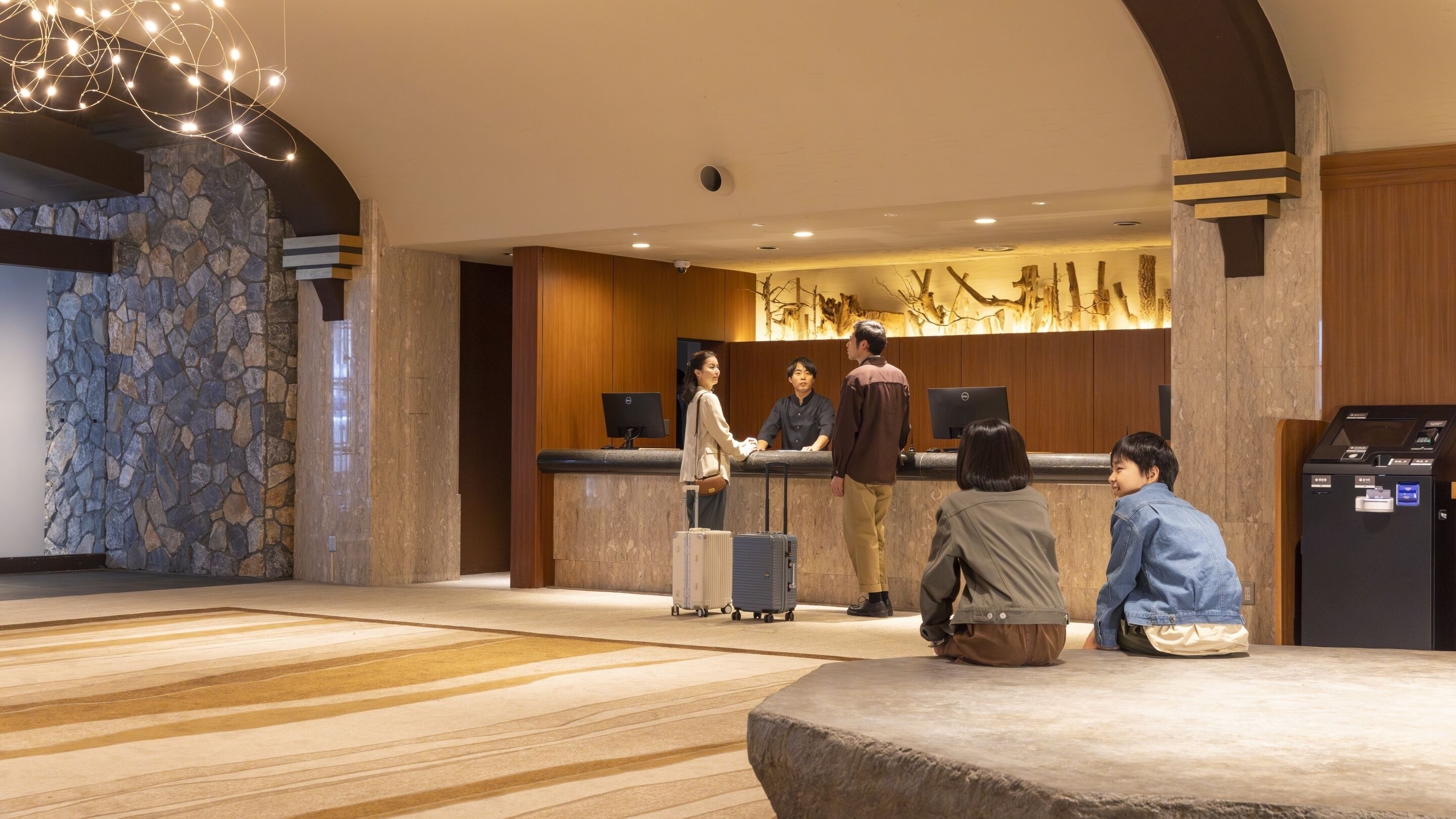 A hotel lobby with a reception desk, a stone wall, and a large chandelier.