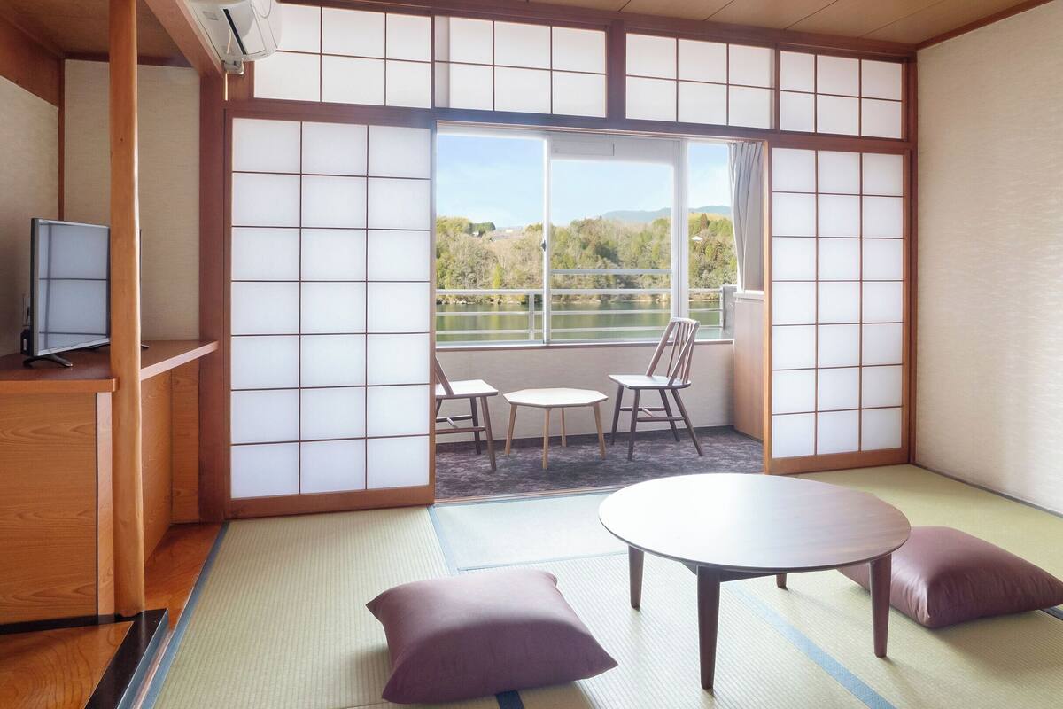 A traditional Japanese room with tatami flooring, a low table with cushions, and a view of a lake through shoji screens.