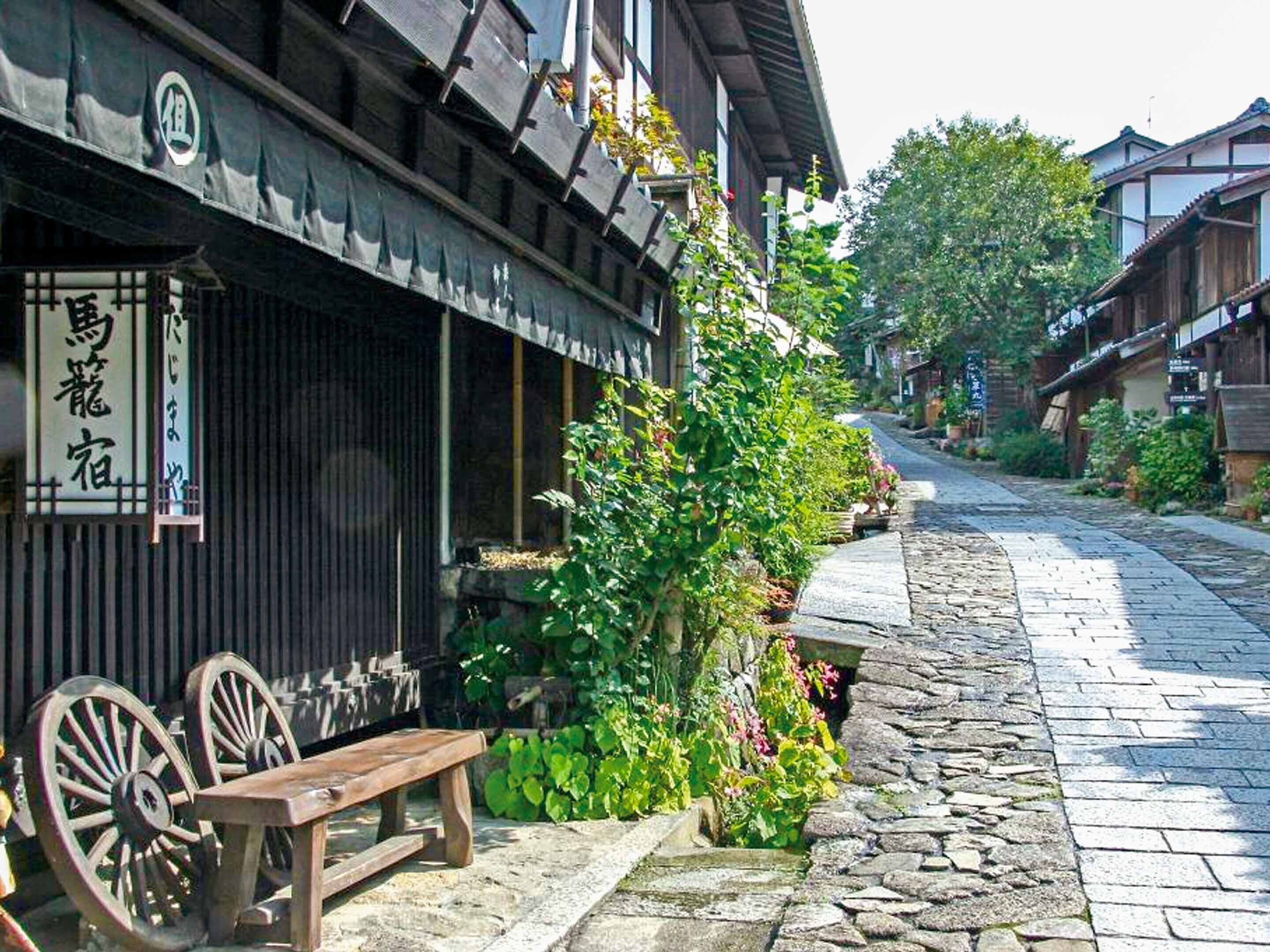 A traditional Japanese building with a wooden exterior, a stone-paved street, and a wooden bench outside.