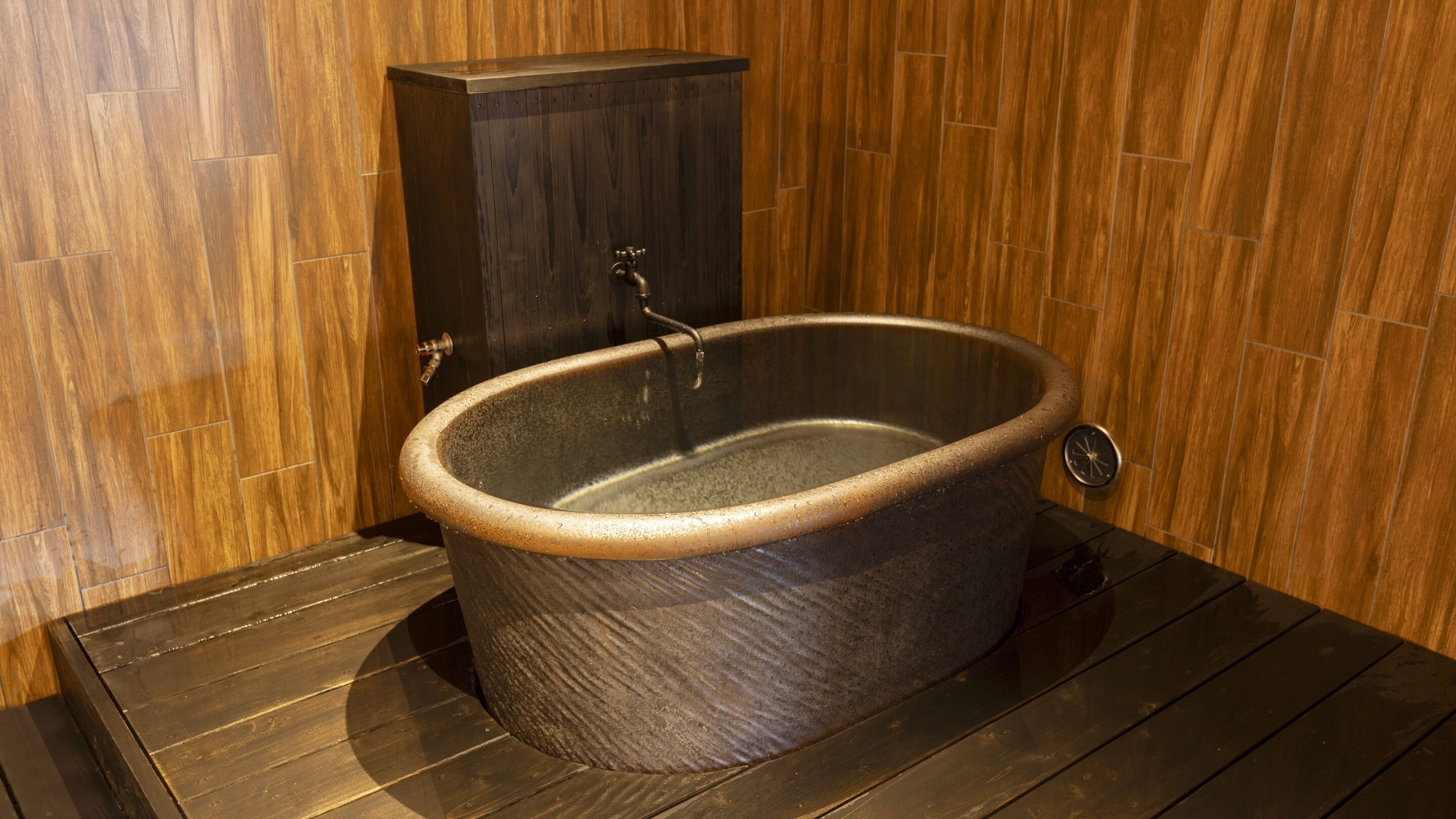 A freestanding bathtub in a wooden-floored room with a dark cabinet.
