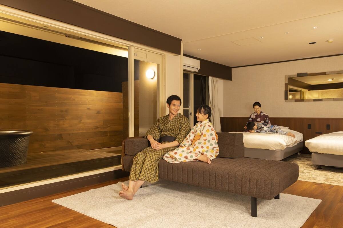 A modern hotel room with a sofa, a bed, a large window, and a mirror.