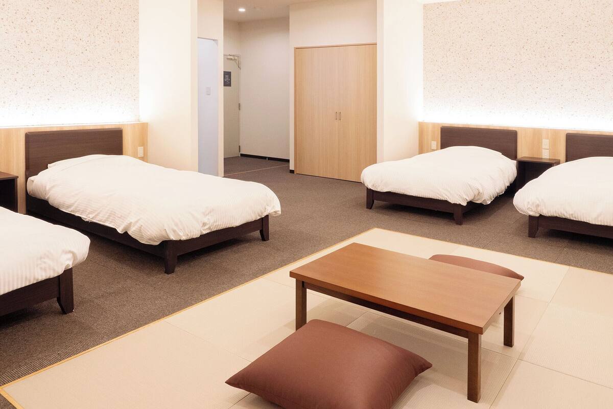 A hotel room with four single beds, a wooden table, and a brown cushion.