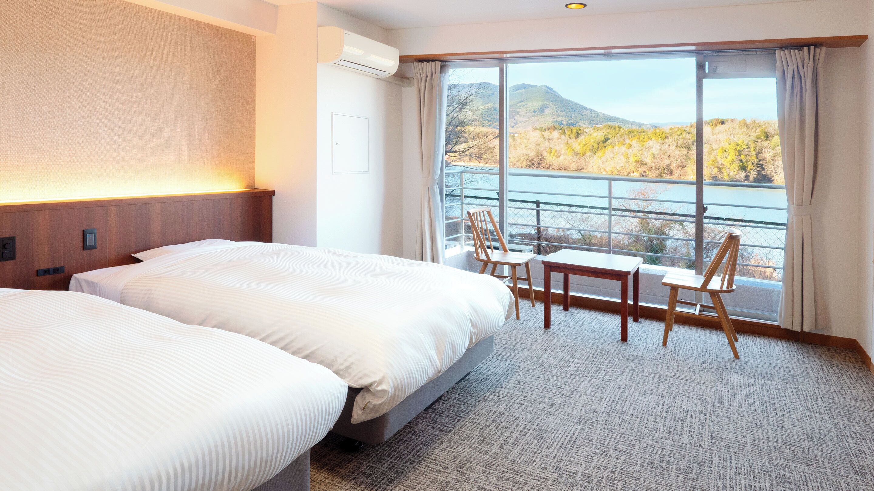 A hotel room with two beds, a table, chairs, a view of a lake, and a mountain in the background.