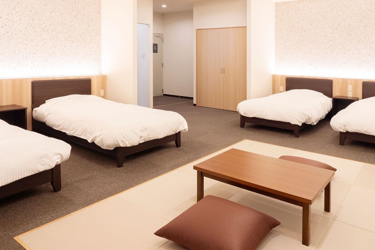 Ein Hotelzimmer mit vier Einzelbetten, einem Holztisch und einer braunen Bank.