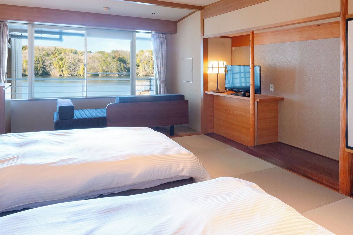 A hotel room with two beds, a TV, and a view of a lake.
