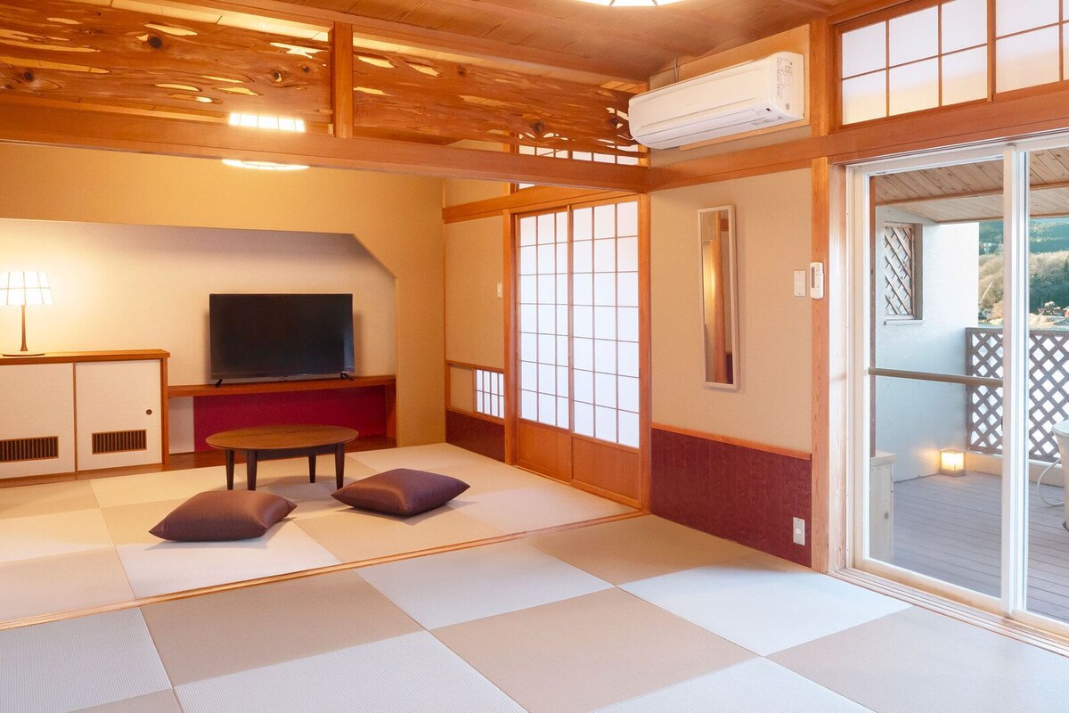 Ein Raum mit Tatami-Matten, einem Fernseher, einem Tisch und Kissen.