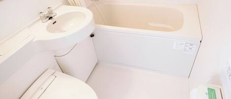 Une petite salle de bain blanche, équipée de toilettes, d’un lavabo et d’une baignoire.