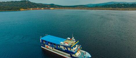 A large riverboat with a blue upper deck and a white lower deck, floating on a calm river.
