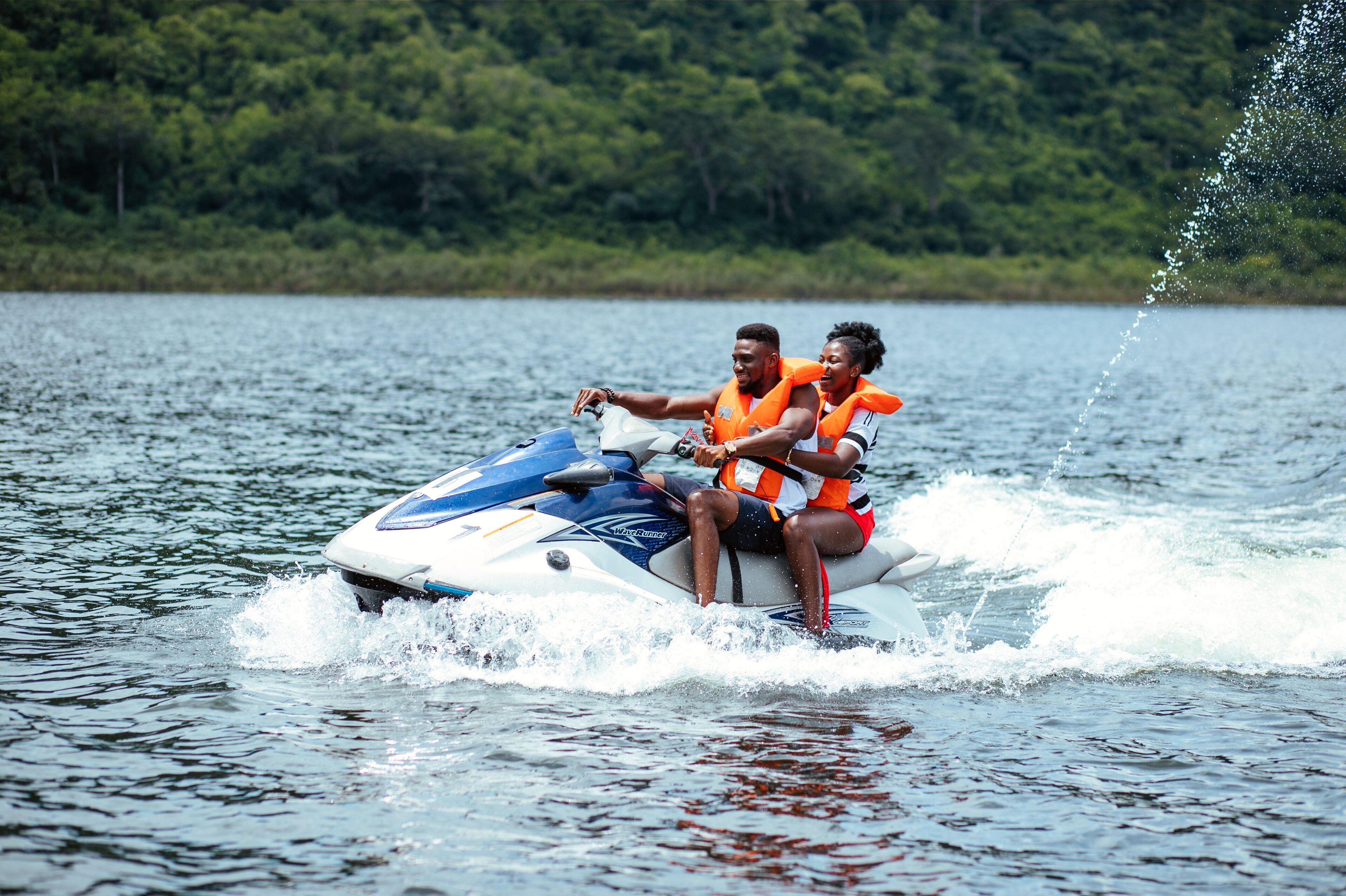 Two people on a watercraft with a forested shoreline in the background.