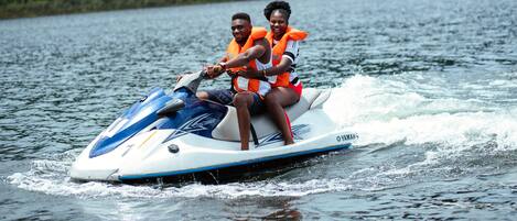 Two people on a jet ski with life jackets, water splashing around.