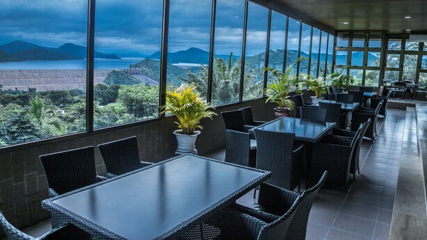 A restaurant with outdoor seating, large windows, and a view of mountains and a body of water. - Volta Hotel Akosombo (Akosombo)
