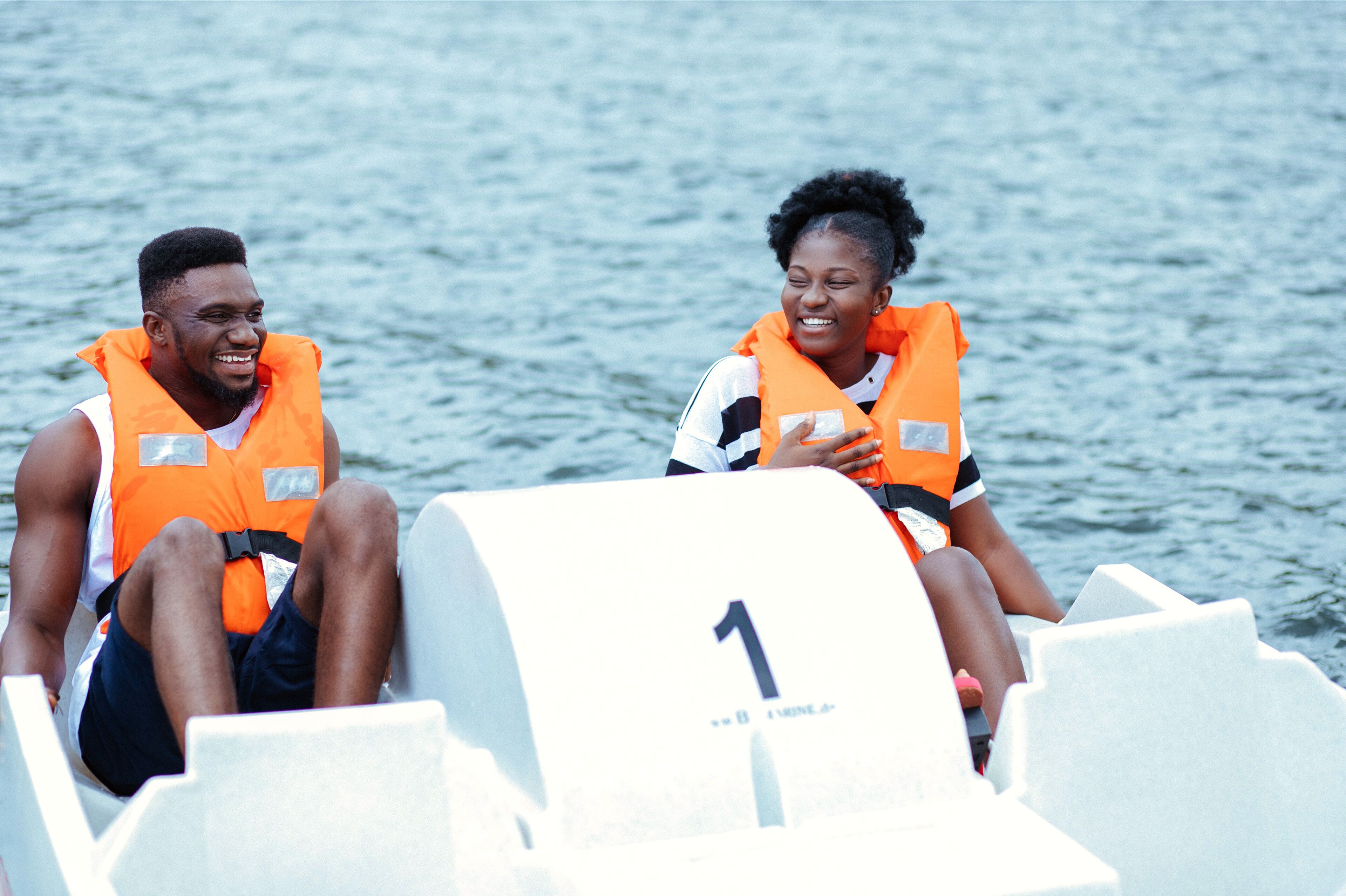 Two people in orange life jackets on a boat with a number '1' on a white structure.