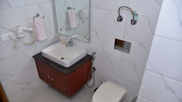 A bathroom with a white sink, wooden cabinet, marble-tiled walls, a toilet, a mirror, and a hairdryer. - Chandertal Regency Hotel & Spa, Manali (Manali)