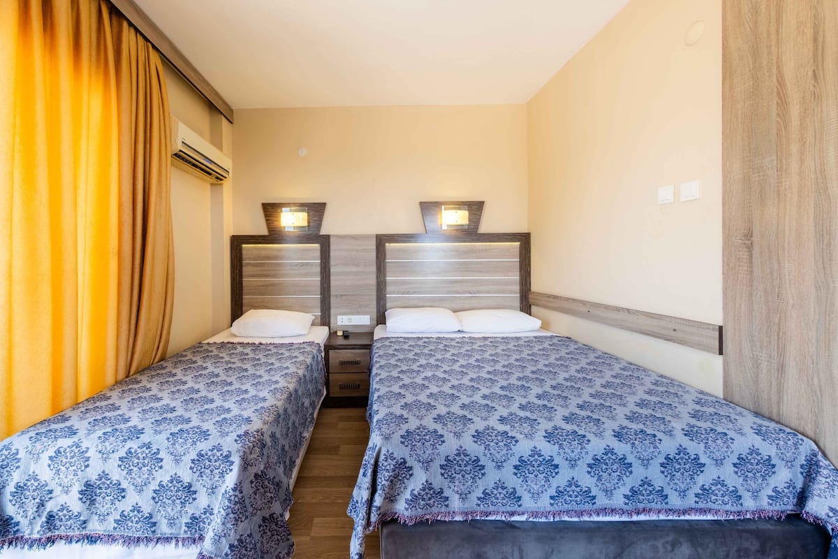 Hotelkamer met twee bedden, een nachtkastje, een airconditioningsysteem en een houten wandpaneel.