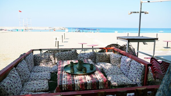 A beachside seating area with a patterned sofa set, a table with metal pitchers, and a view of the beach and ocean.