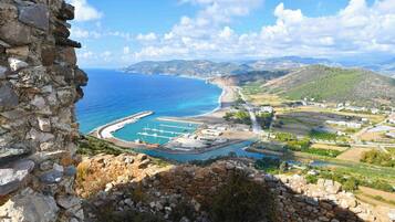 Blick auf die Küste mit einer Steinmauer, einem Yachthafen und einer hügeligen Landschaft.