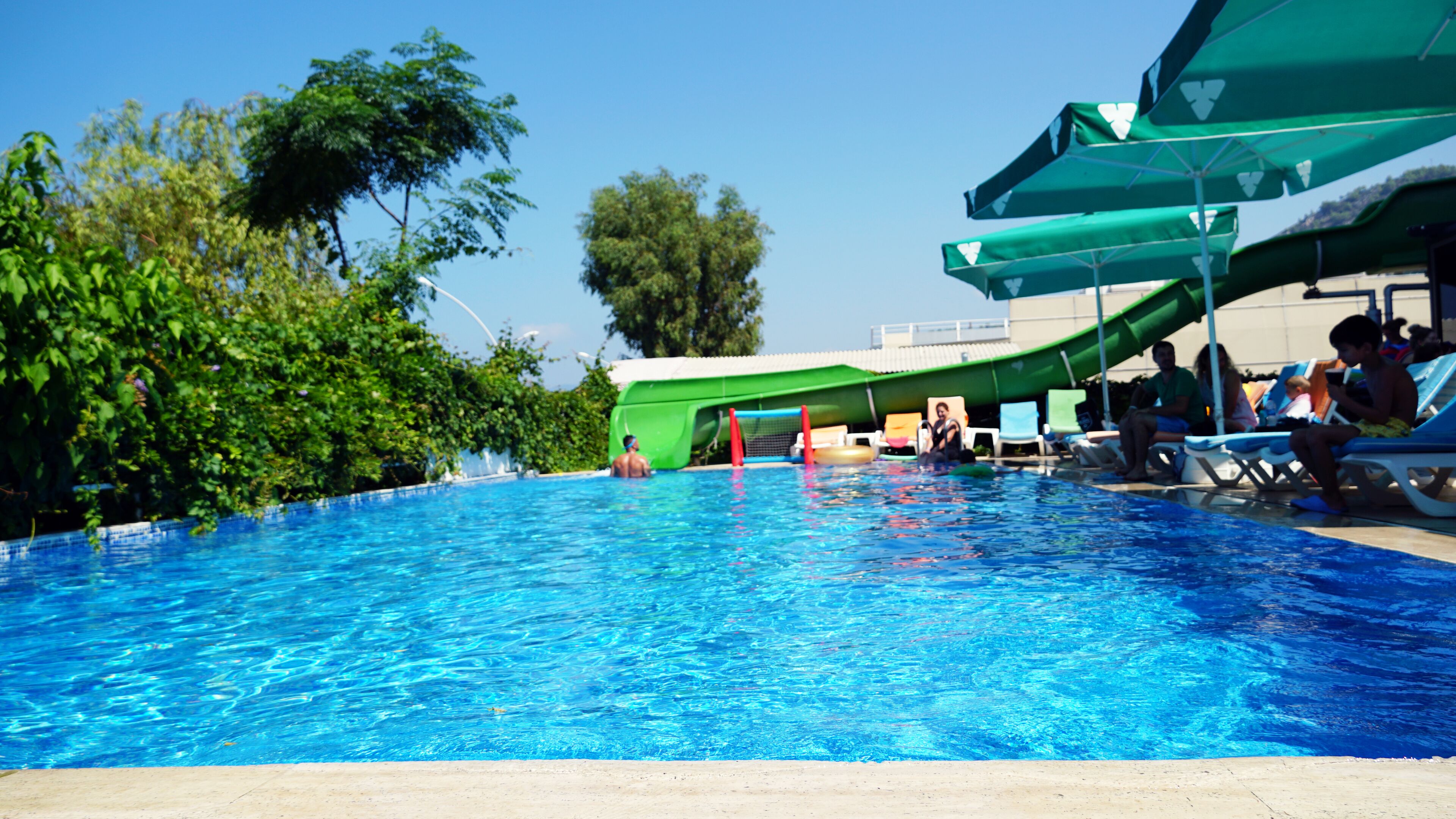 Une piscine avec un toboggan, des chaises longues et des parasols.