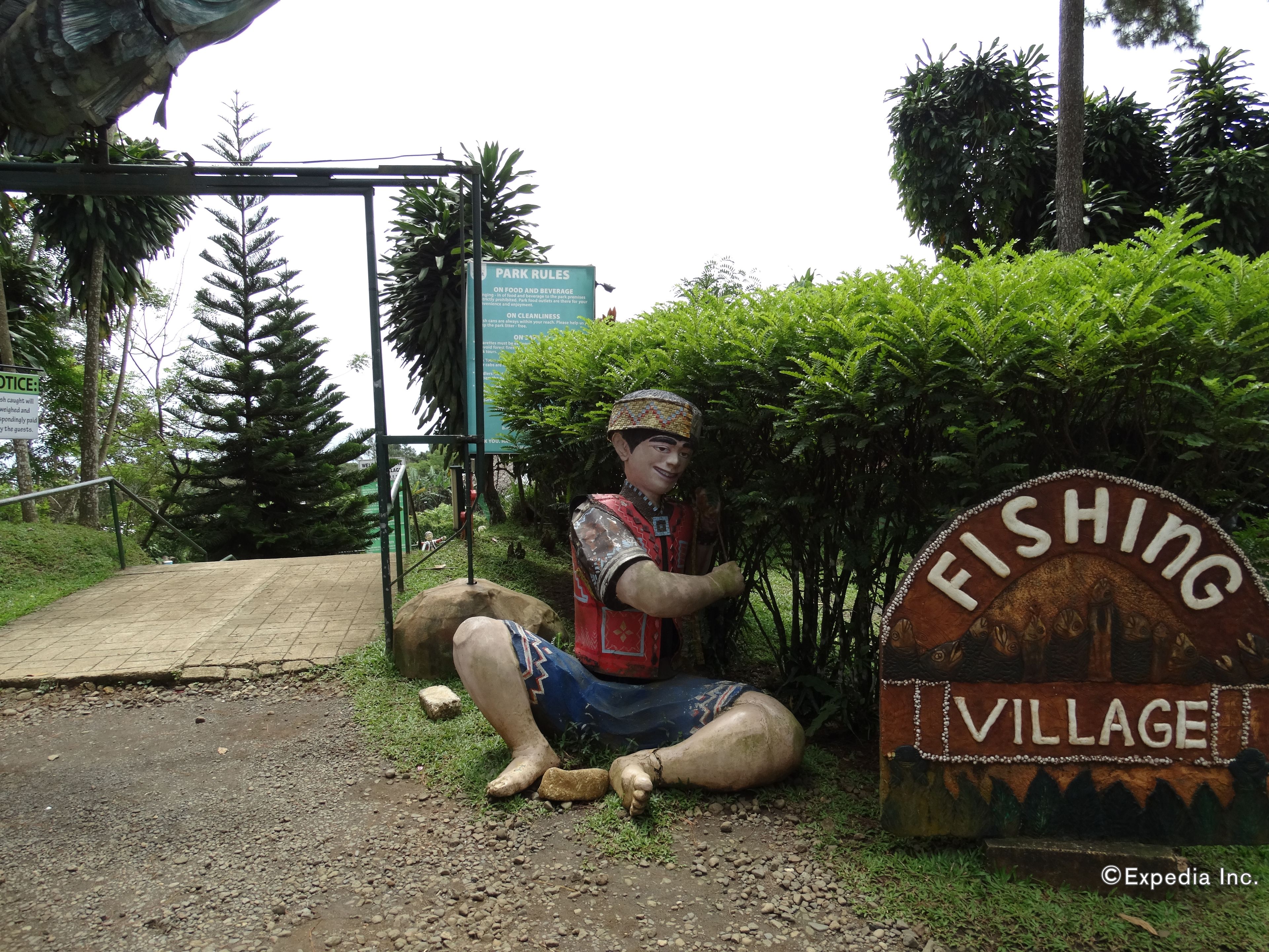 A sign for Fishing Village with a statue of a man fishing.