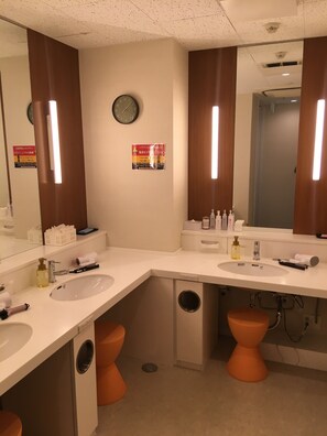A modern bathroom with two sinks, a mirror, a clock, and a toilet.