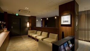 A reception area with a wooden reception desk, a seating area with beige sofas, a framed picture on the wall, and a digital display board. - First Cabin Akasaka (Tokyo)
