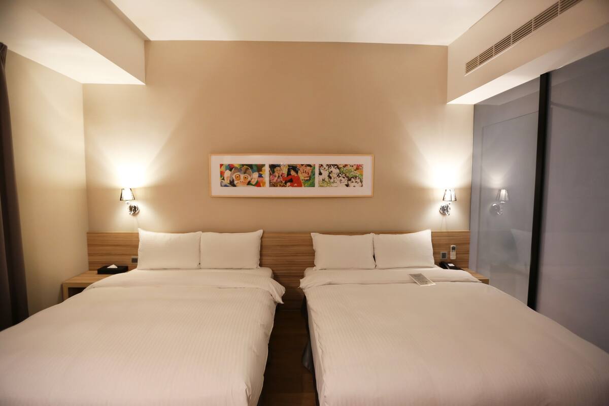 A hotel room with two beds, a wall-mounted artwork, bedside lamps, and a wardrobe.