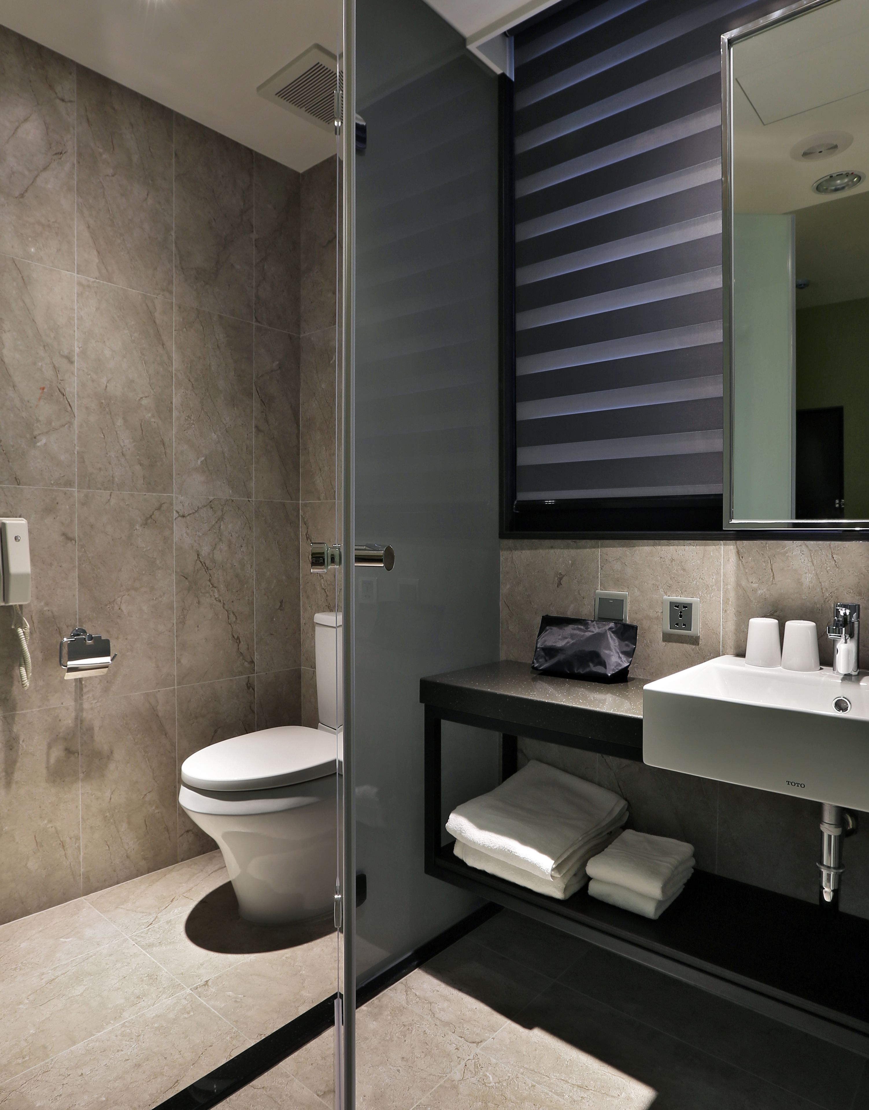 Un baño moderno con inodoro, cabina de ducha de vidrio, lavabo con toallero y espejo con persianas.