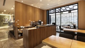 A modern hotel lobby with a wooden reception desk, a coffee station, and a seating area with tables and chairs. - Miller Inn (Taichung)