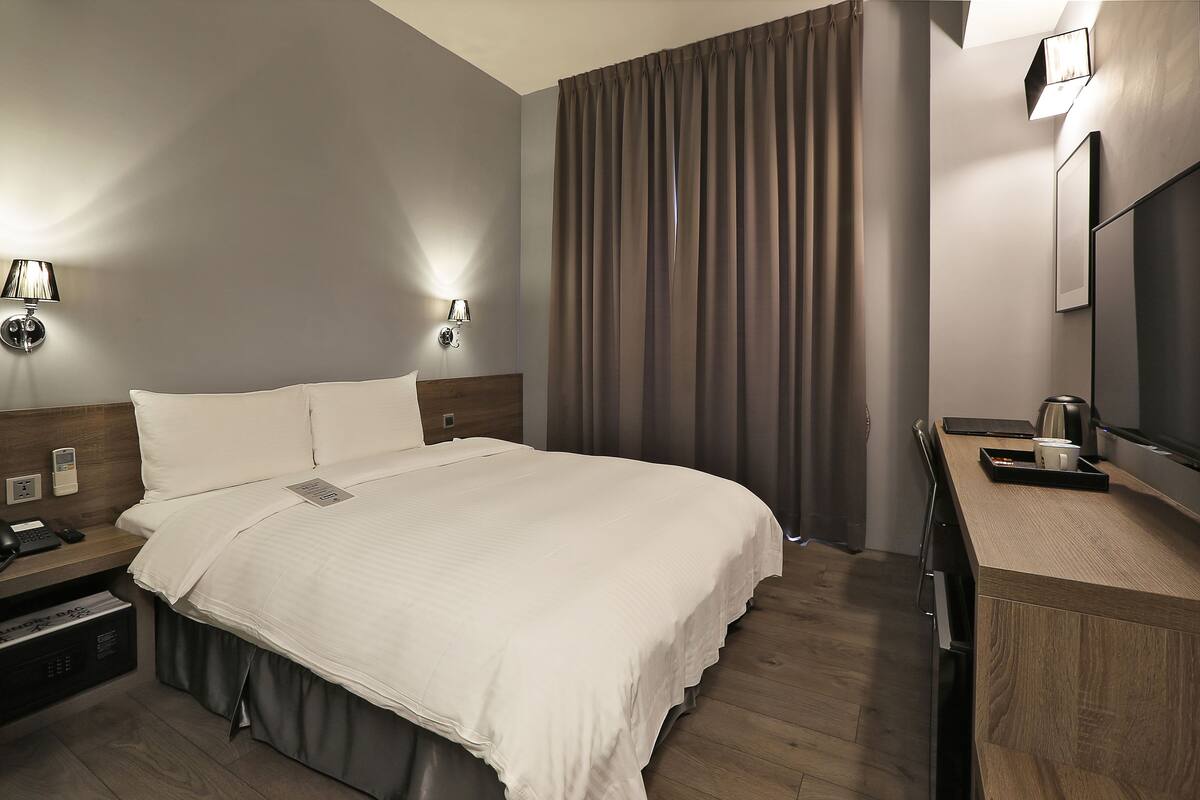A modern hotel room with a large bed, bedside tables, a desk, and a mirror.