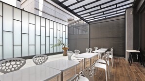 A modern indoor dining area with white tables and chairs, a large potted plant, and a view of a building with large windows. - Miller Inn (Taichung)