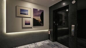 A modern elevator with a control panel, a wall-mounted light strip, and three framed pictures. - Miller Inn (Taichung)