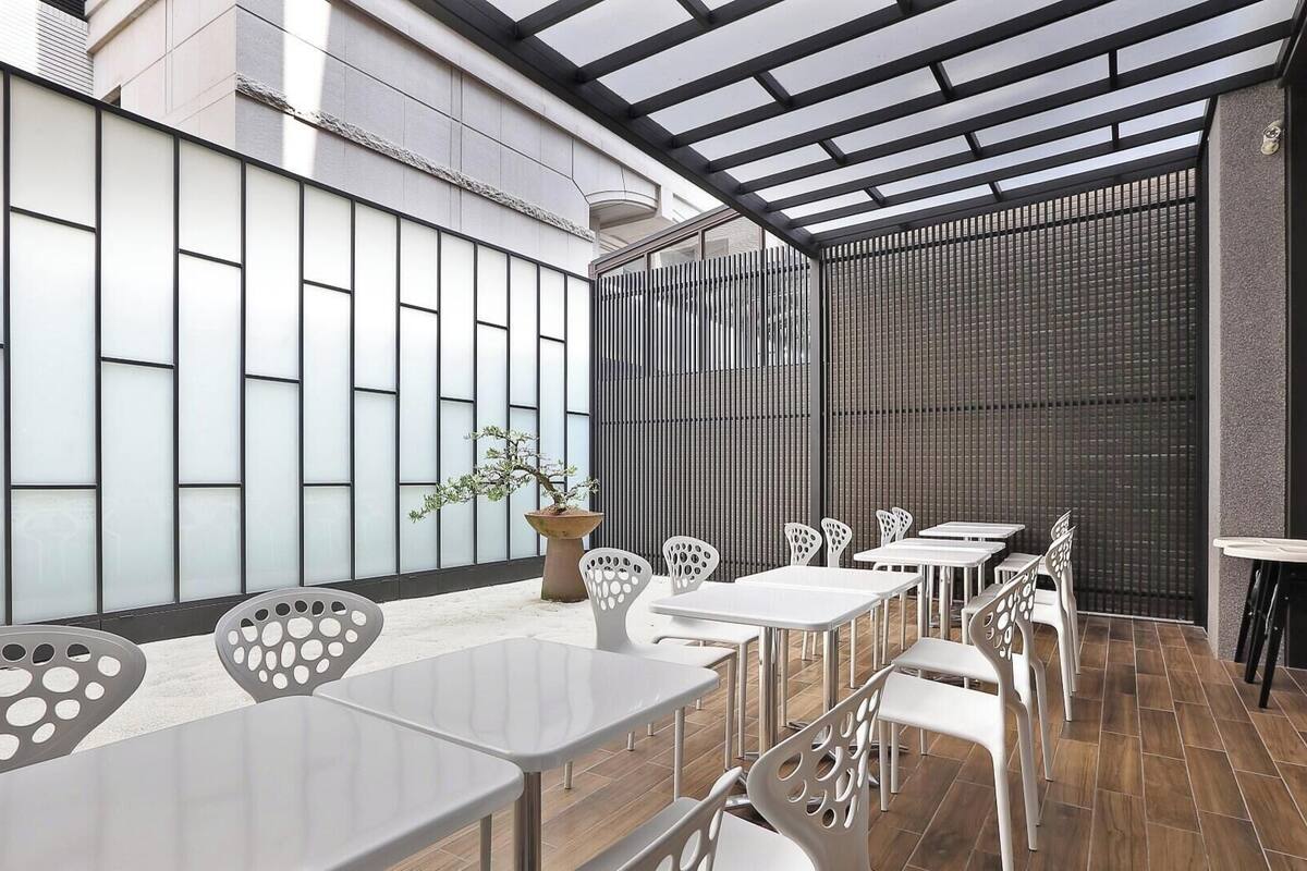 A modern outdoor seating area with tables and chairs, a potted plant, and a view of the building's exterior.