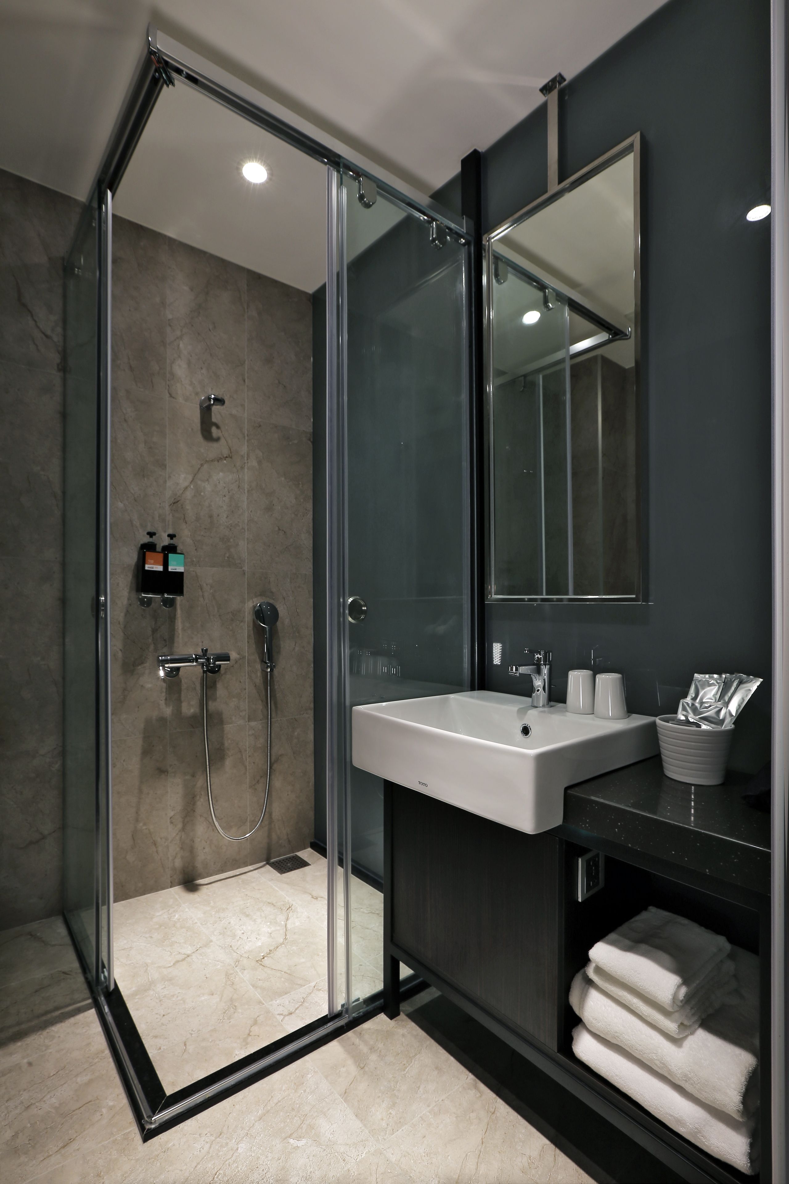 A modern bathroom with a glass-enclosed shower, a white sink, and a large mirror.