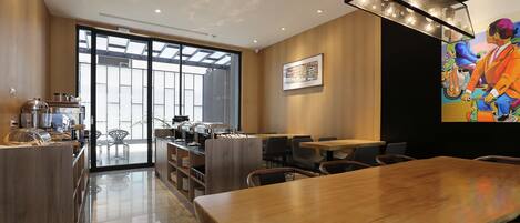 Una cafetería moderna con interior de madera, un mural grande y una puerta de cristal que da a un área de asientos al aire libre.