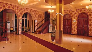 Un vestíbulo espacioso con alfombra roja, columnas ornamentales y una imponente escalera.