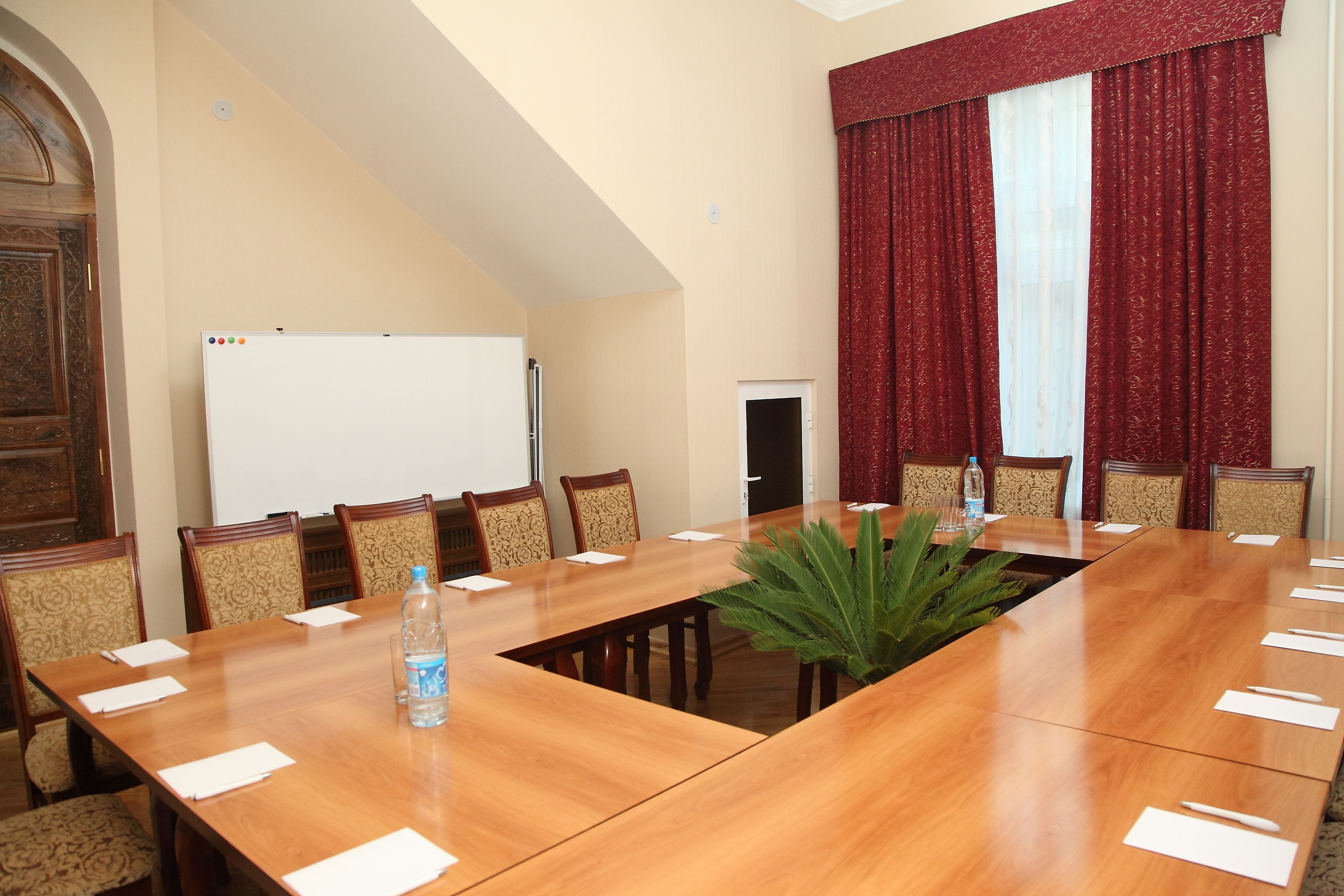 A conference room with a long table, chairs, a whiteboard, and red curtains.