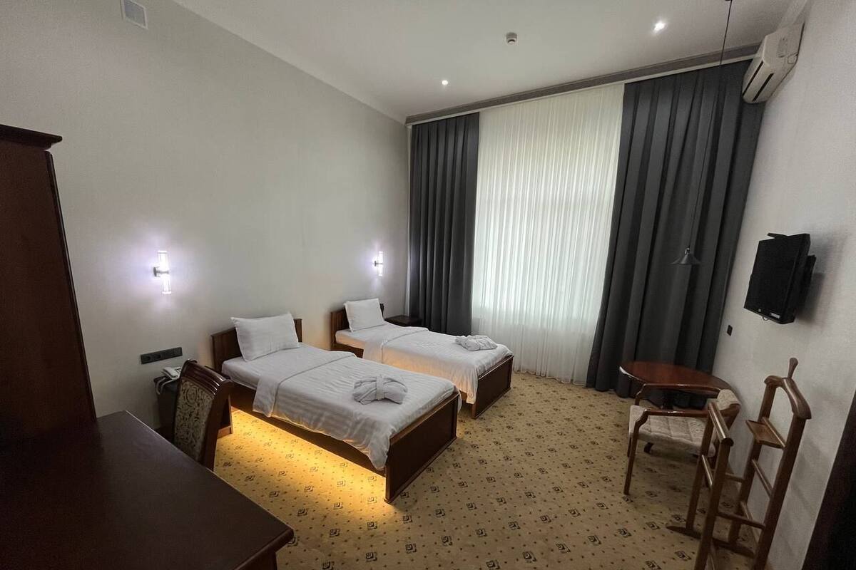 A hotel room with two single beds, a desk, a chair, a TV, and a window with curtains.
