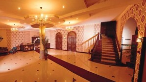 Un hall majestuoso con piso pulido, una araña, una escalera y paredes con diseños.