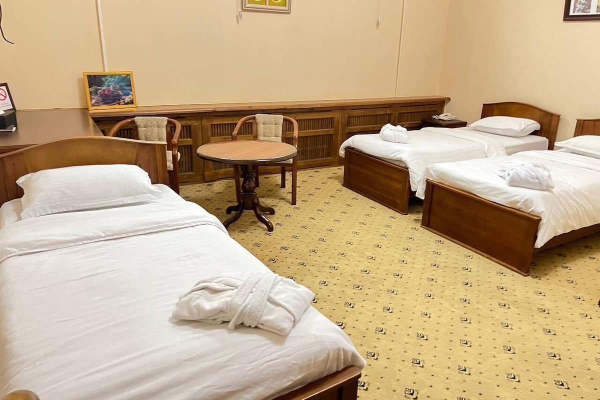 A hotel room with three single beds, a round table, and a chair.