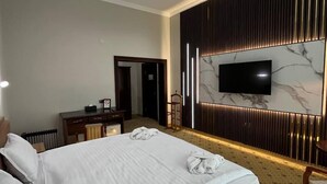 Habitación de hotel con una cama grande, un escritorio y un televisor fijado en una pared de mármol.