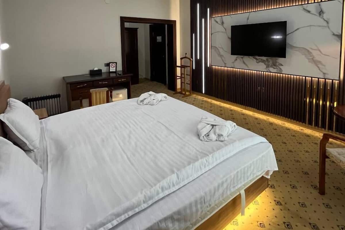 A hotel room with a large bed, a desk, and a television mounted on a marble wall.