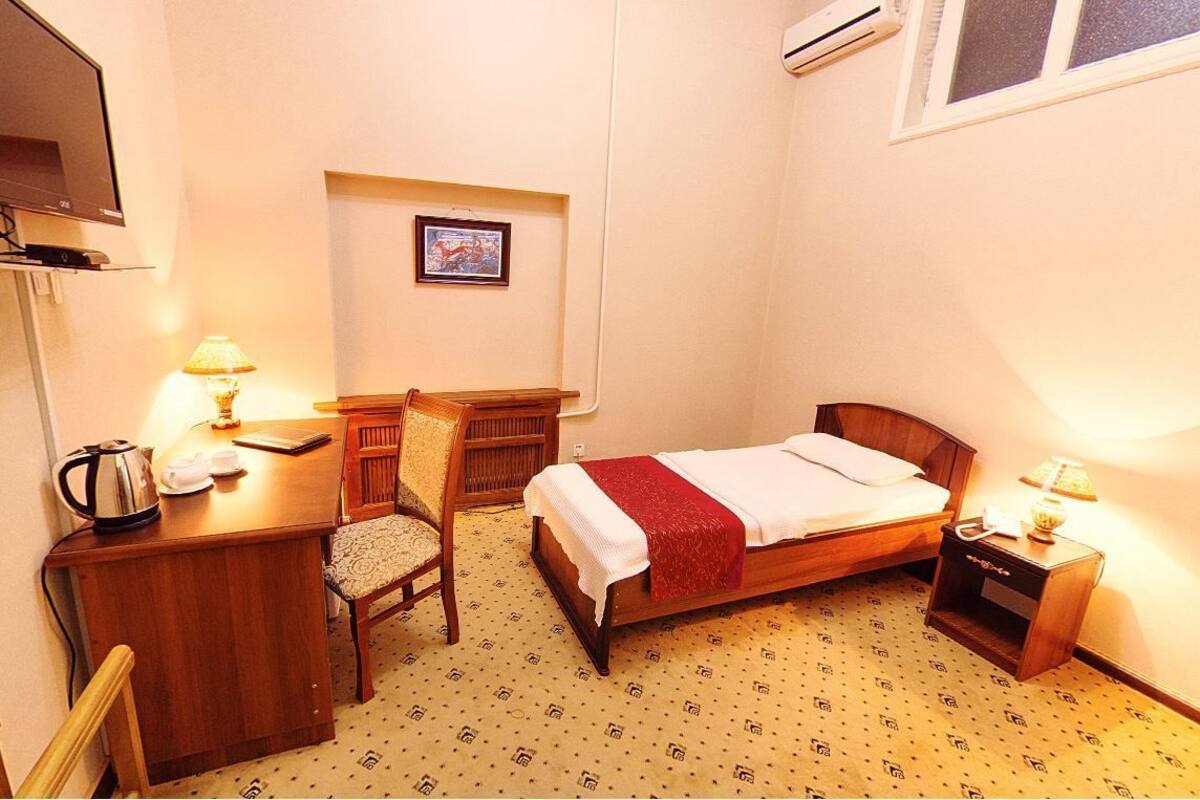A small hotel room with a bed, desk, chair, and a television.