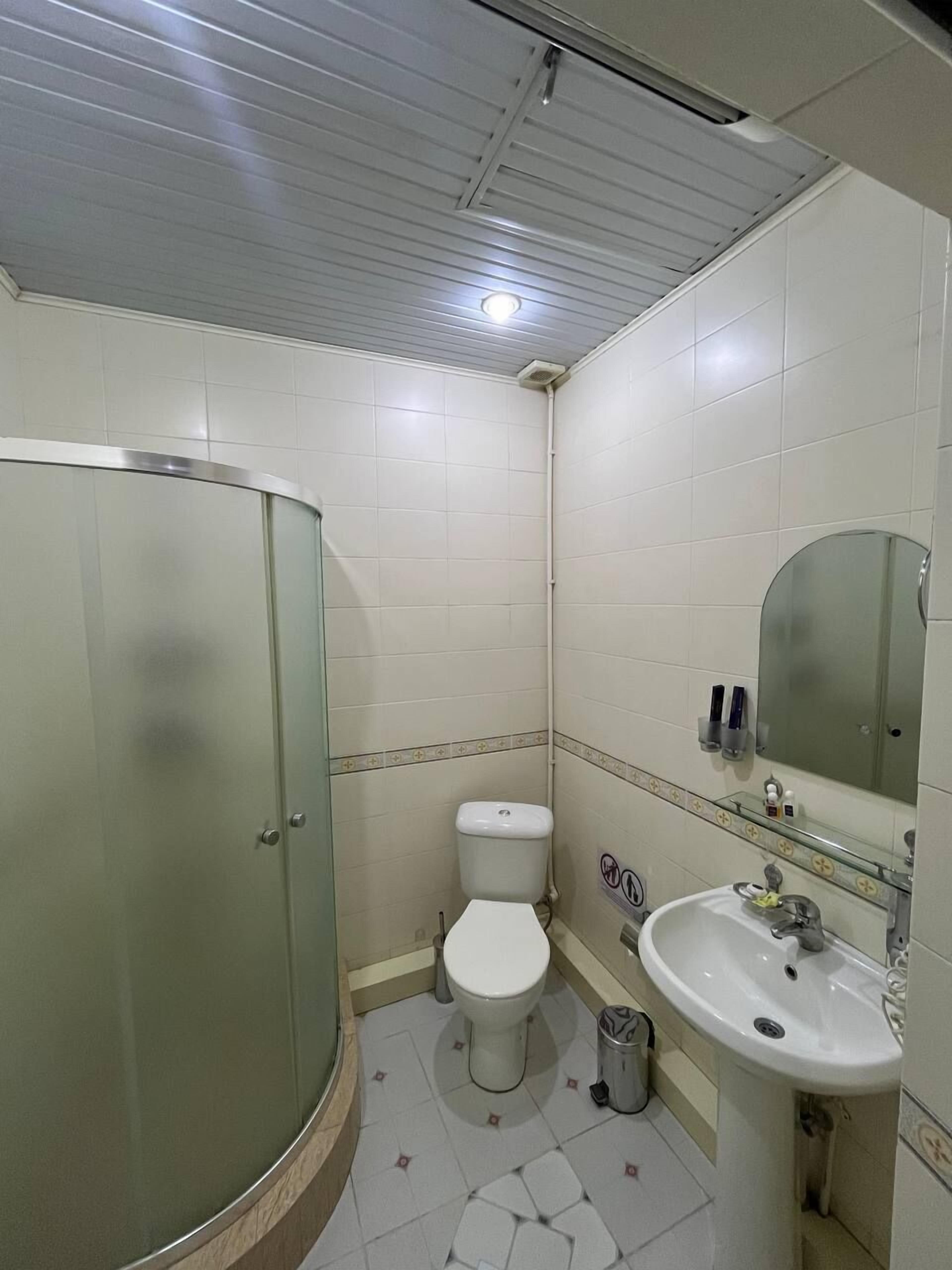 A bathroom with a glass shower enclosure, a toilet, and a sink with a mirror.