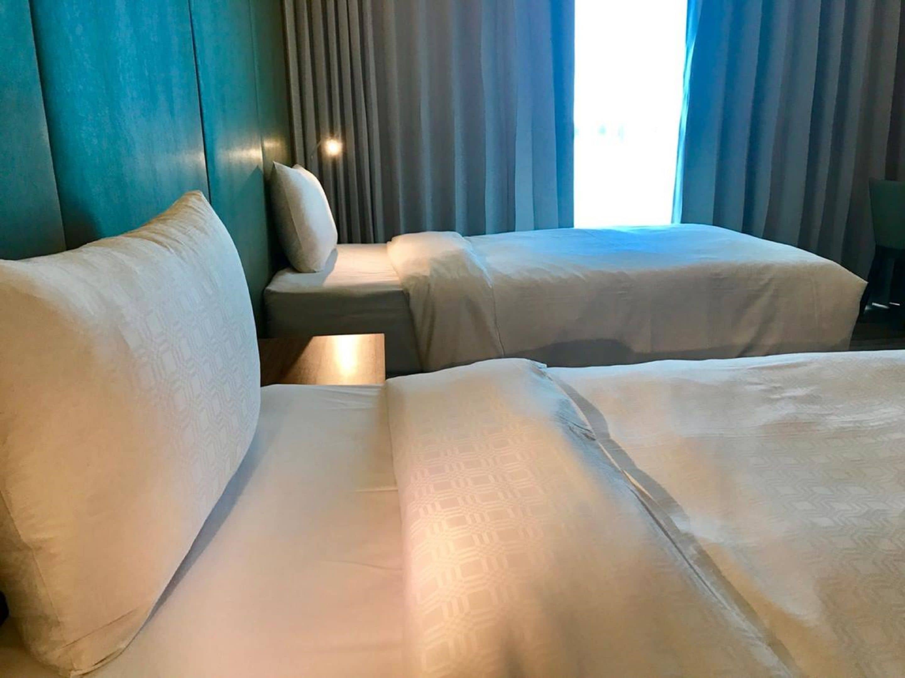 Una habitación de hotel con dos camas, una mesita de noche y un ventanal con cortinas.