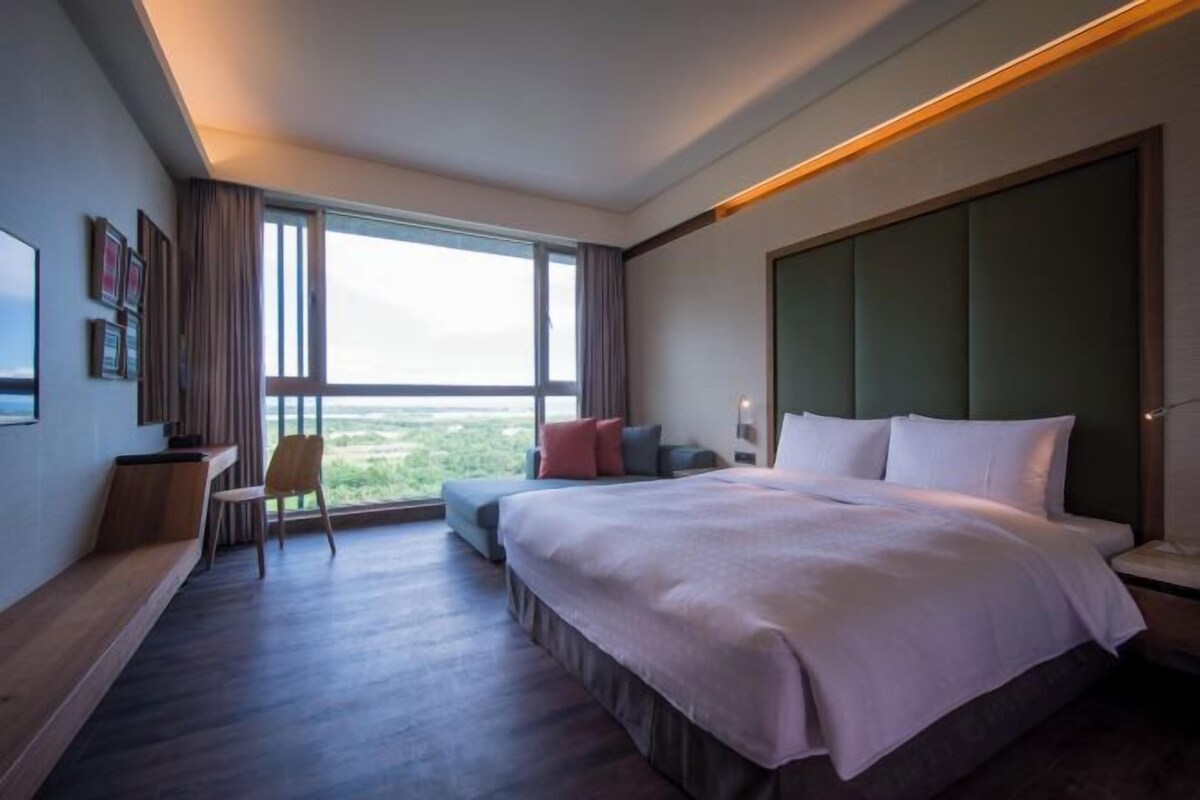 A modern hotel room with a large bed, a seating area with a view, and a large window.