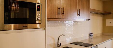 Una cocina moderna con microondas integrado, pileta de acero inoxidable y muebles de madera.
