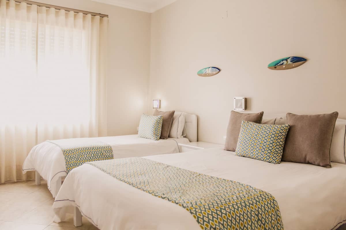 Habitación de hotel con dos camas, paredes color beige y un ventanal con cortinas.