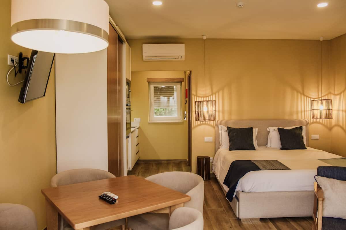 Habitación de hotel con cama, lámparas de noche, escritorio con silla y una mesita con control remoto.