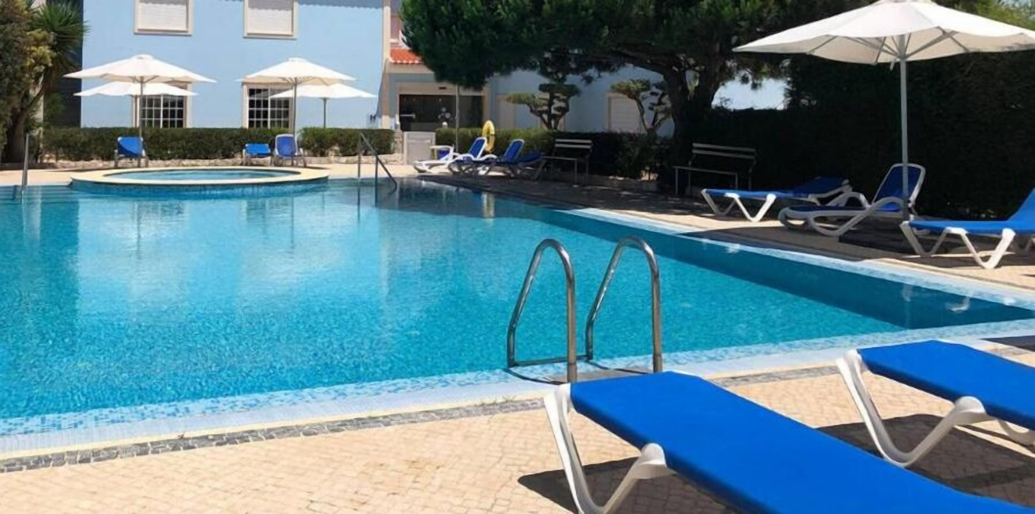 Una piscina con agua azul, rodeada de sillas de descanso y sombrillas.