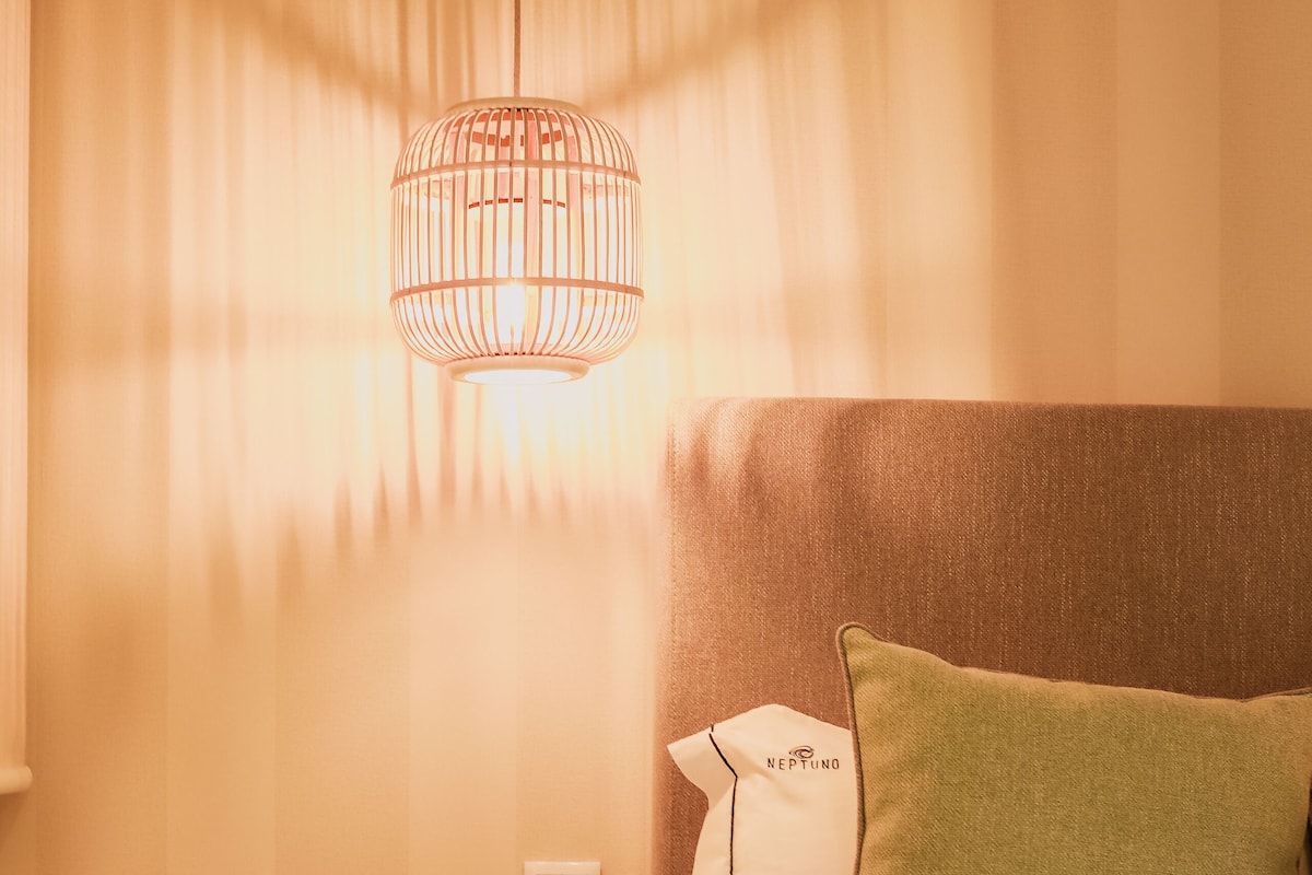 Un dormitorio ordenado con cama, mesita de noche y lámpara colgante.